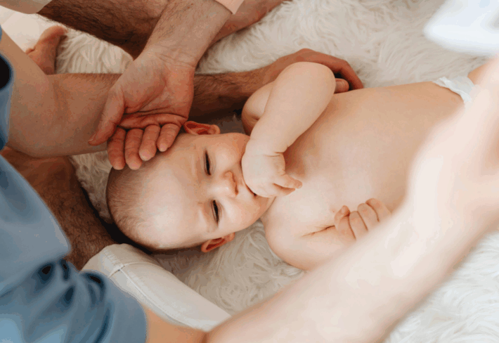 An infant lies on his back while two bodywork practitioners assess his sensory processing ability.
