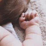 A baby lies on a blanket. We can only see his head and arm. His fist is clenched as if he is tense.